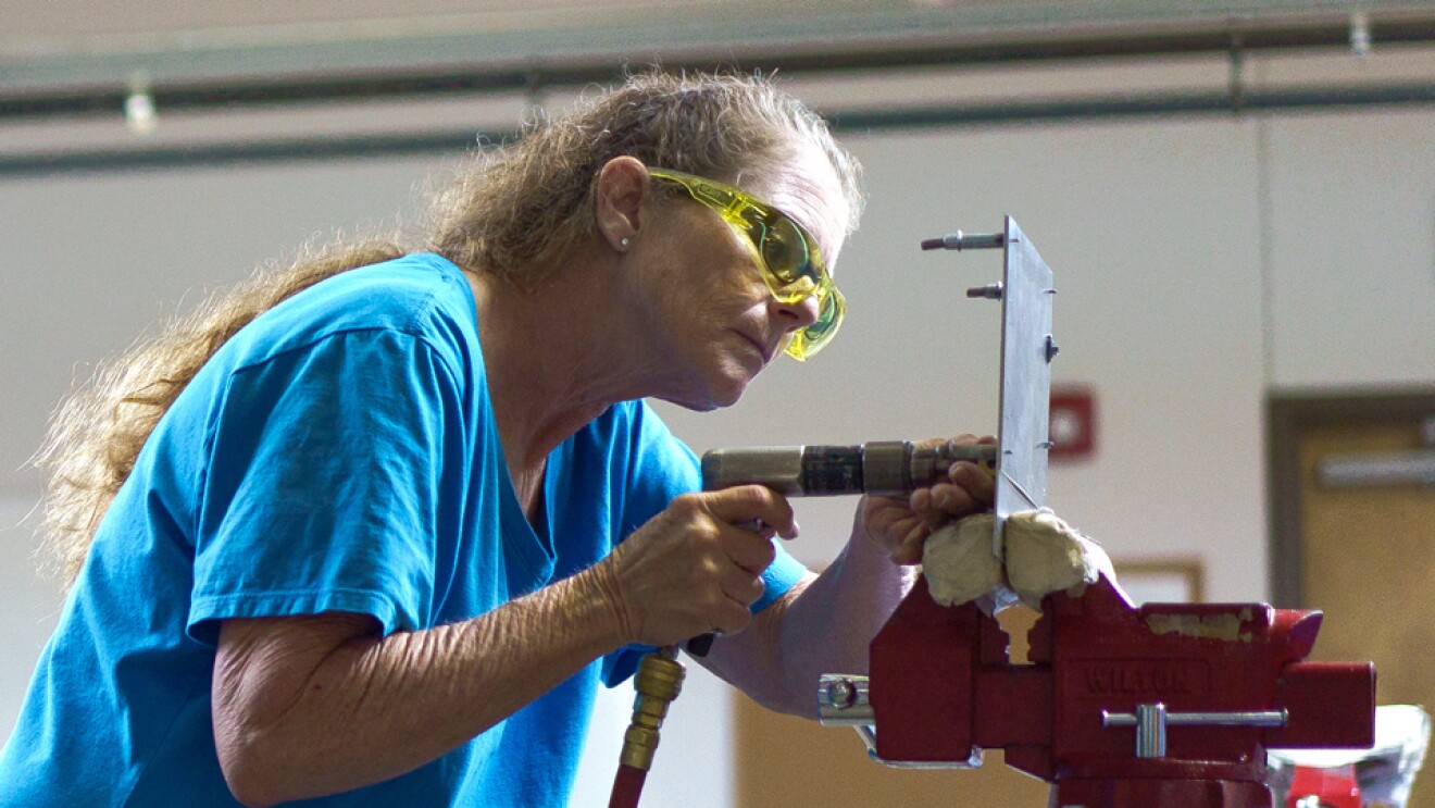 一个女人在一个蓝色的t恤和安全眼镜液压工具适用于金属板和斜向工作台虎钳。