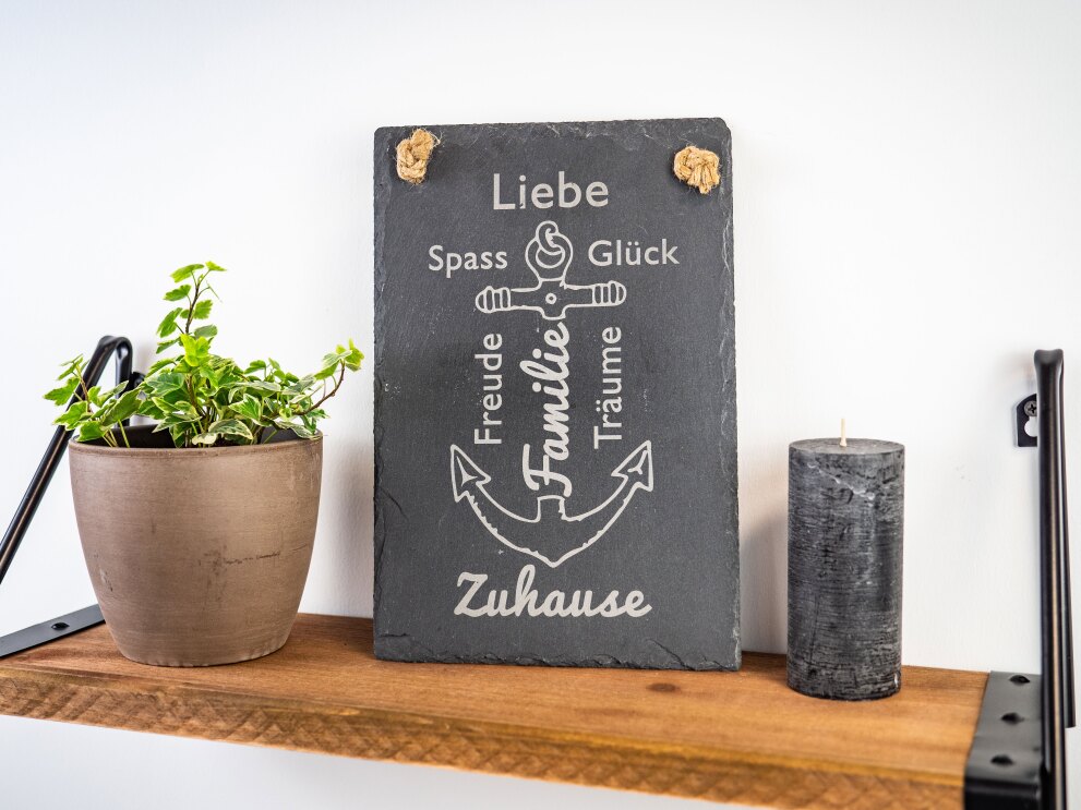 Auf einem Holzregal steht eine Schieferplatte mit einem weißen Anker und Stichworten "Familie, Zuhause, Glück, Spass"
