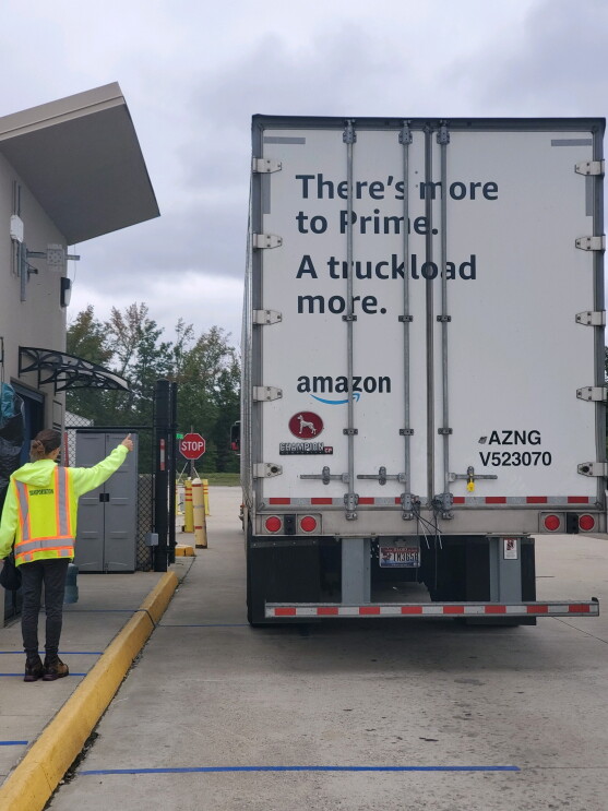 An Amazon employee in safety gear and mask gives a "thumbs up" to an Amazon truck as it drives off, full of customer orders.