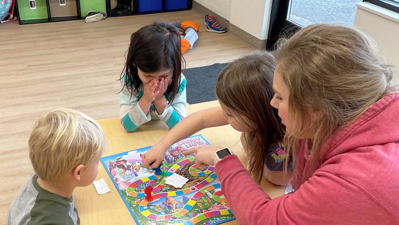 A photo of a teacher playing a board game with three students.