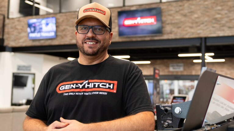 Man wearing GEN-Y HITCH branded shirt and cap standing in automotive showroom