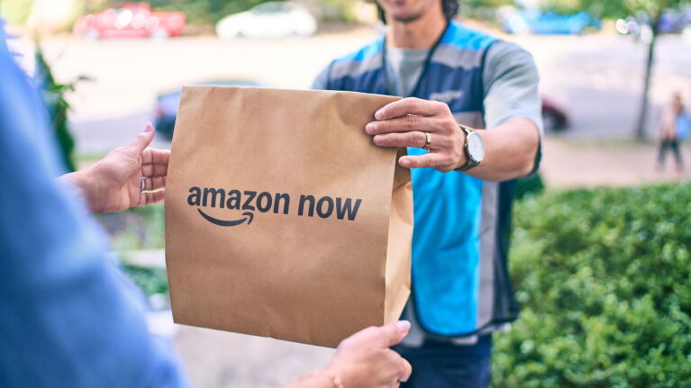 Delivery person handing Amazon Now paper bag to customer outdoors