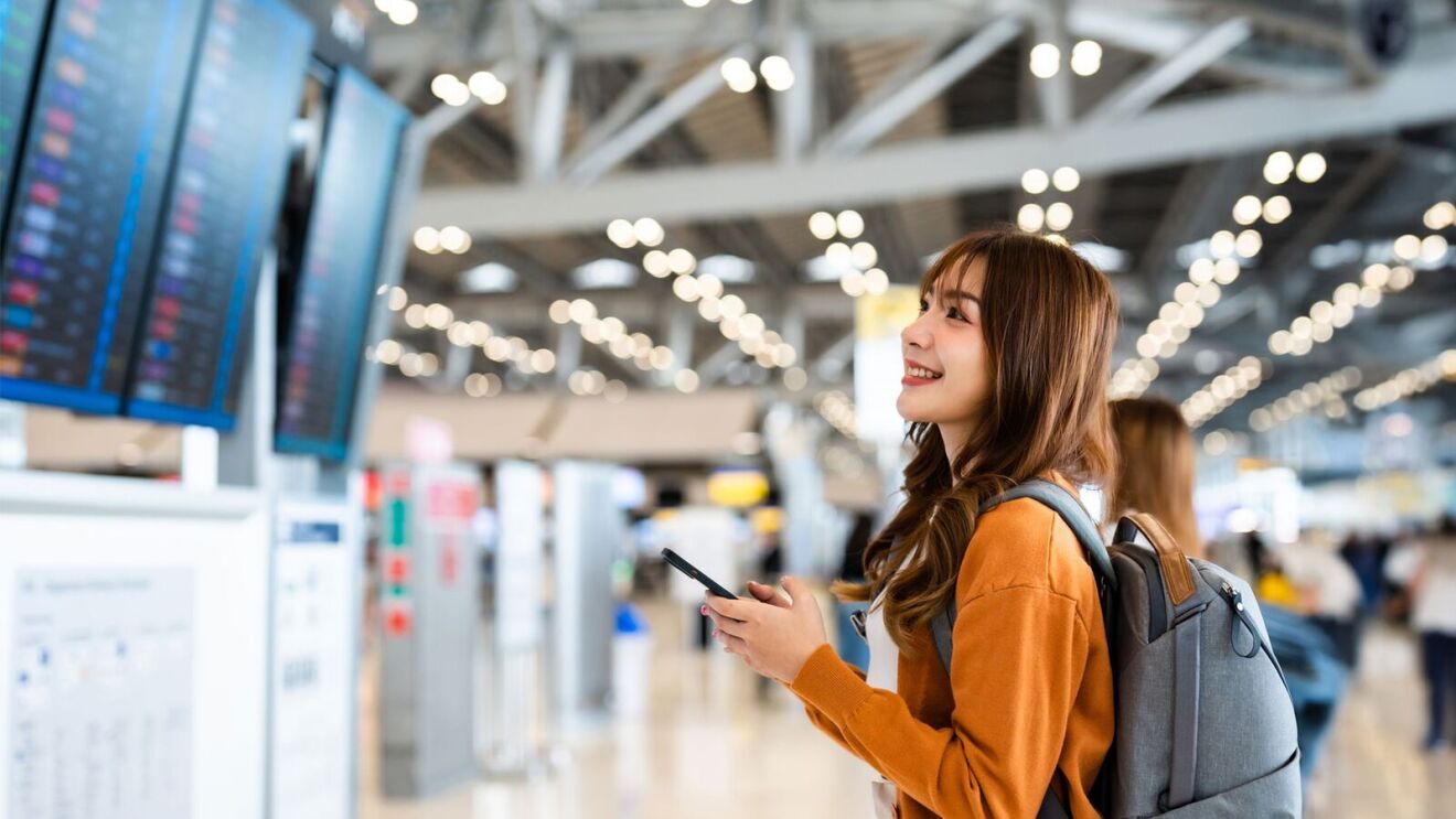 An image of a woman in an airport looking at flight schedules on TV screens.