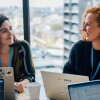 Two women sitting at a desk in front of laptops