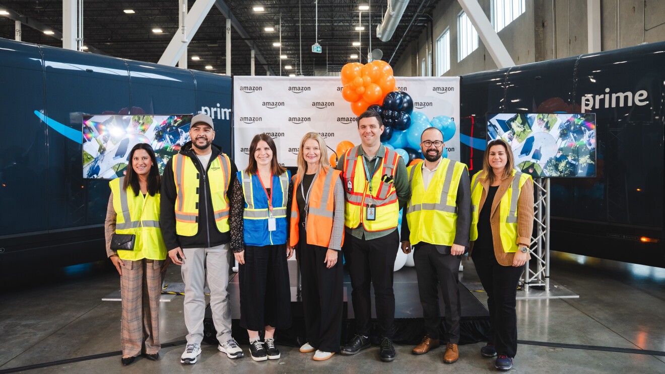 Image of a group of people in yellow vests posing in front of Amazon x Rivian delivery vans