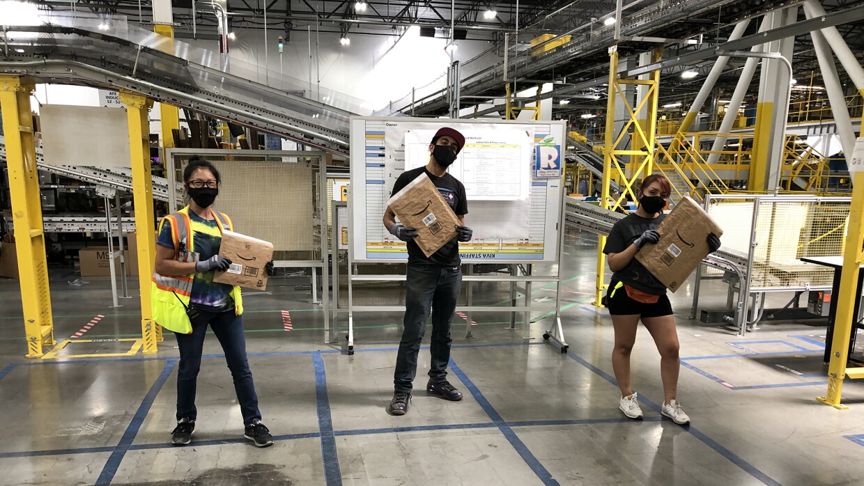 Three Amazon associates stand in a fulfillment center, holding the new recyclable mailer. 