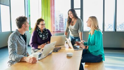 四个人围着一张桌子工作,电脑摆在他们面前。