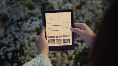 Mains tenant une liseuse Kindle affichant une interface en français sur fond de marguerites