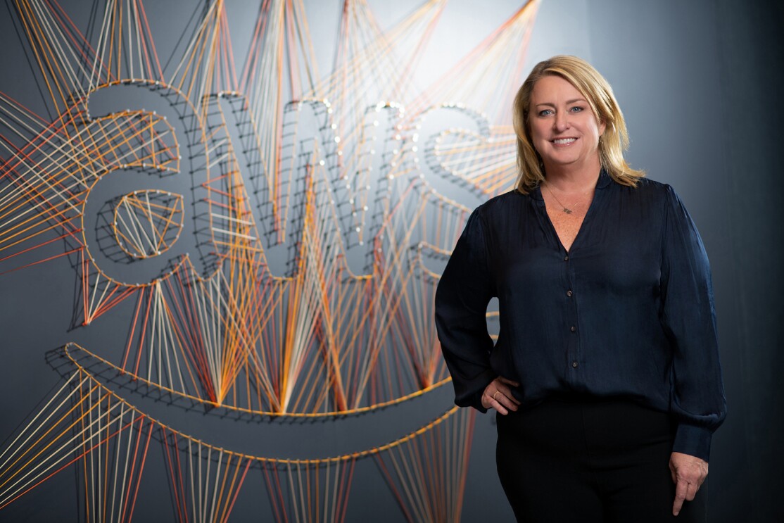 An image of a woman smiling for a photo in front of a wall that says "AWS" in string. 