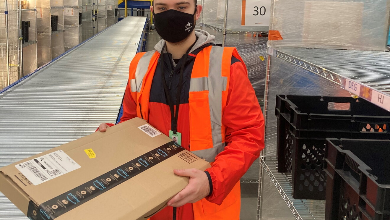 Finlay Shouler, Sortation Associate at Amazon's delivery station in Sheffield , pictured holding an Amazon parcel next to a conveyor belt.