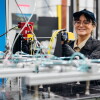 Female fulfillment center worker smiling while operating manufacturing equipment with robotic arms
