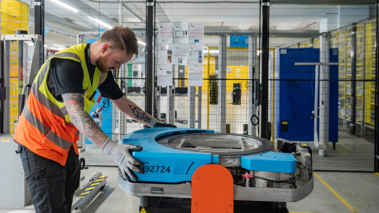 Amazon worker scanning a blue automated mobile robot in a distribution facility