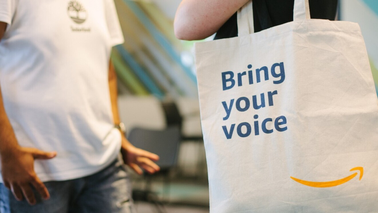 Immagine che mostra persone all'interno di una sede Amazon con shopper in primo piano con scritta "Bring your voice"
