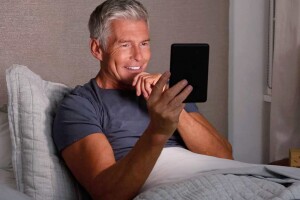 Man in bed reading on his Kindle.