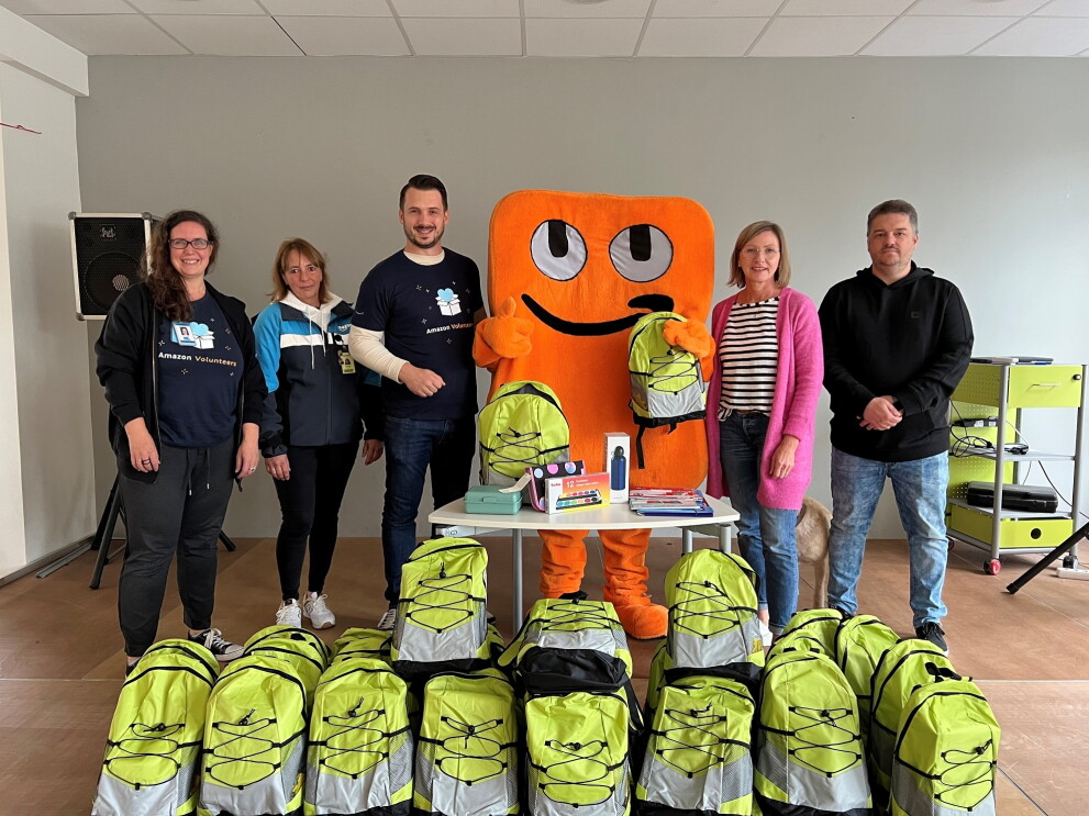 Amazon Mitarbeiterinnen und Mitarbeiter und Maskottchen Peccy mit grünen Back to School Rucksäcken