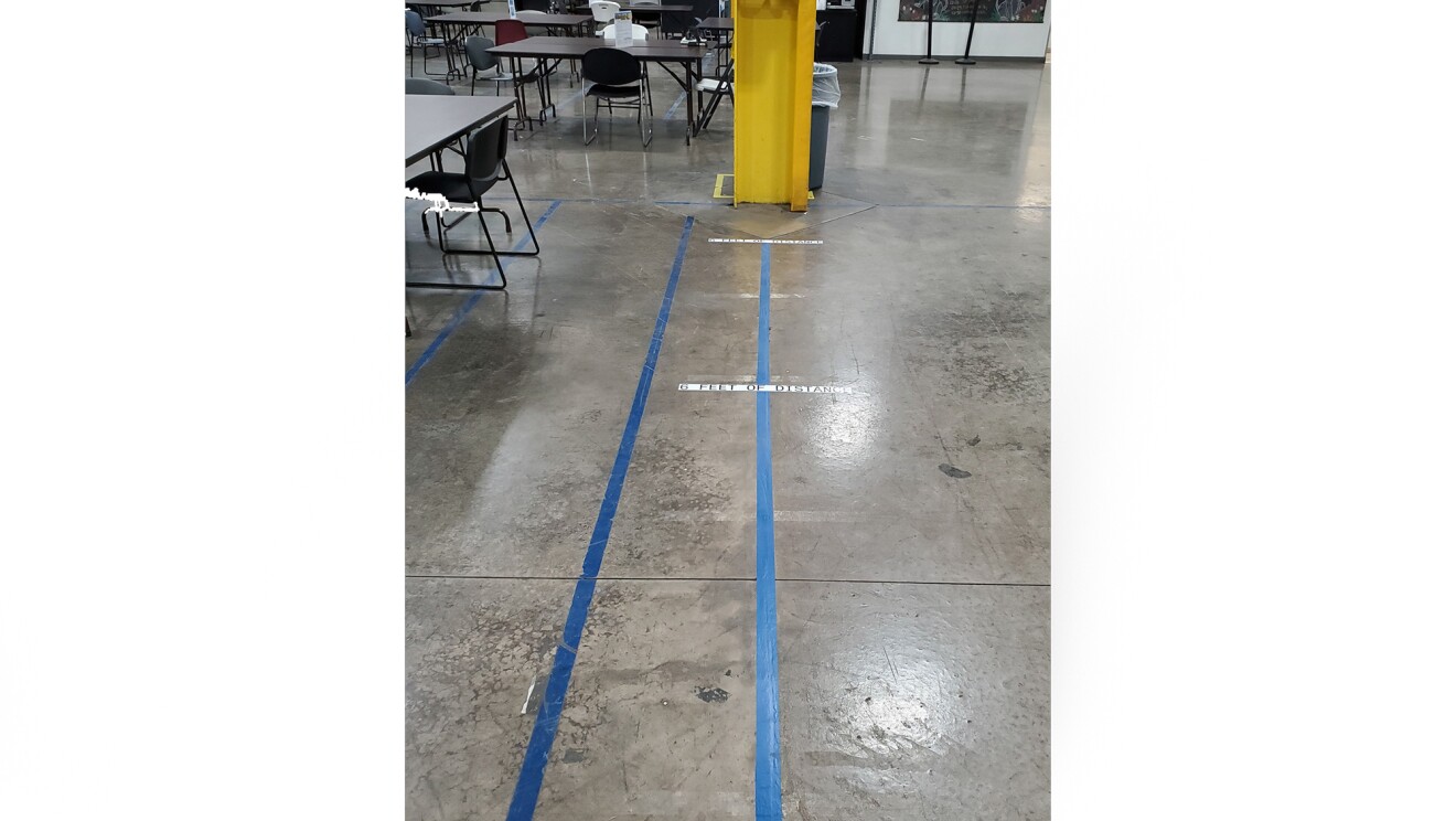 Zegar czasu w centrum realizacji Amazon, ze znakami na podłodze pokazującymi, gdzie współpracownicy powinni stać podczas używania, i gdzie odległość 6 stóp jest od zegara czasu.