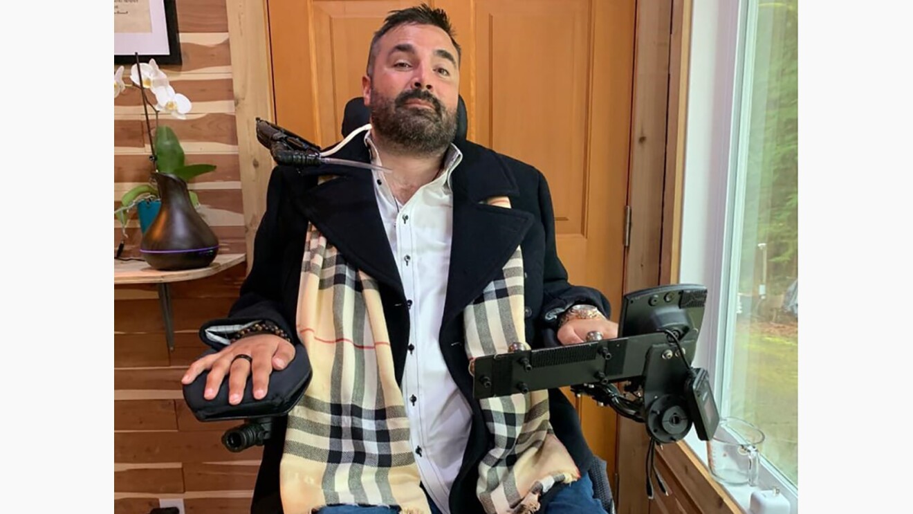 Tyler sitting in his motorized wheelchair, next to a window.