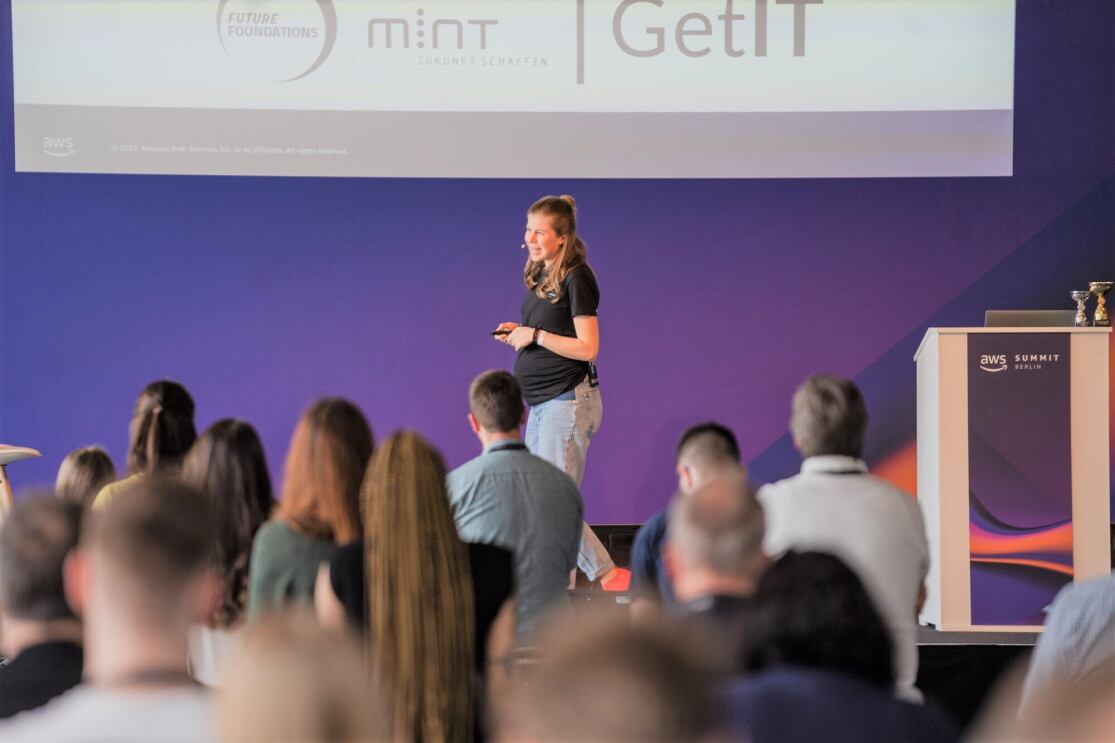AWS GetIT Botschafterin Anja Blank auf der Bühne beim Erklären auf dem AWS Summit 2022 in Berlin worum es bei AWS GetIT geht.