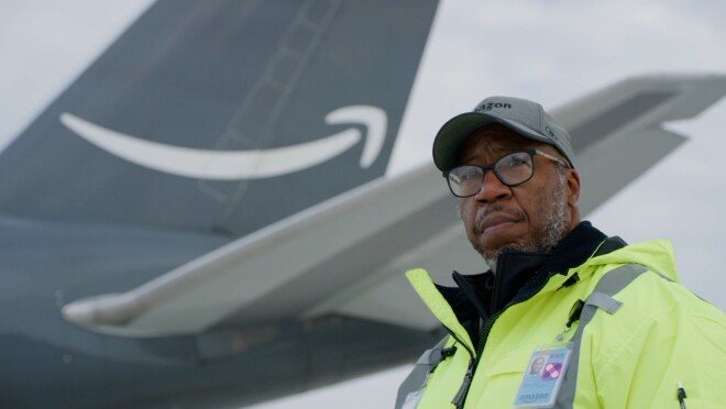 一名身穿黄色安全夹克、头戴亚马逊帽的男子站在一架印有亚马逊微笑标志的飞机前,