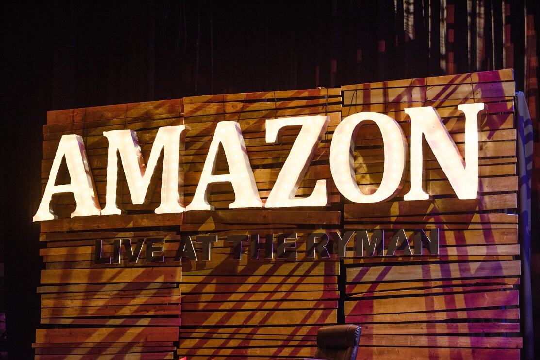 Amazon "Live at the Ryman" stage sign from Nashville event. The sign is three panels wide, each panel made up of pieces of horizontal wood that are fit together. There are lighted letters that spell "Amazon," with "Live at the Ryman" below.