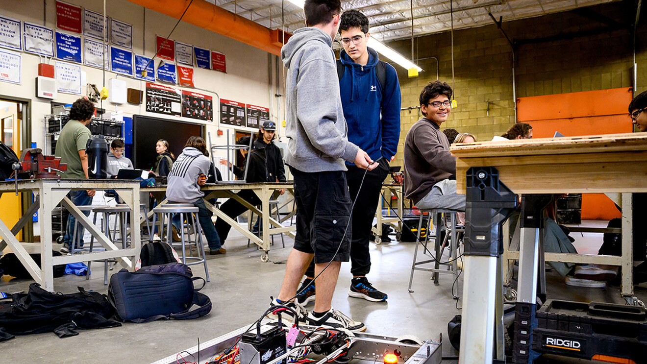 A photo of two students standing in front of a robot in a high school robotics lab.