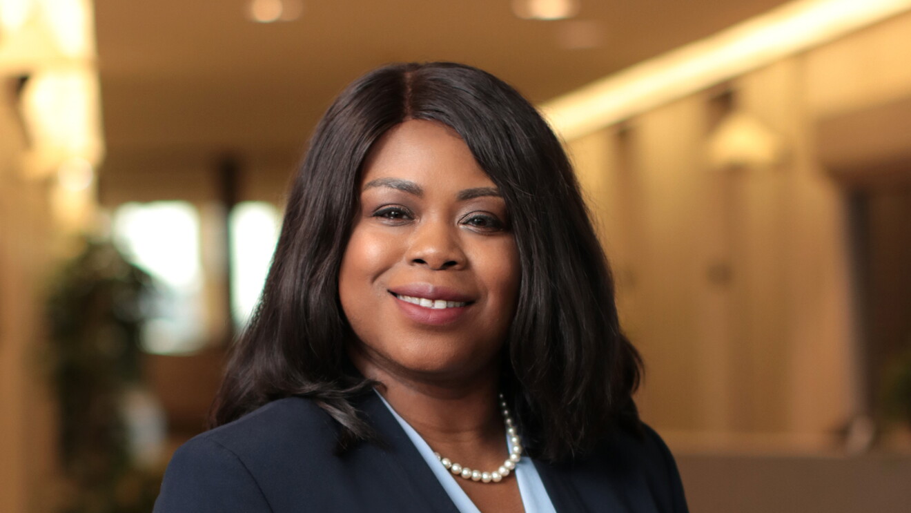 An image of a woman smiling for a professional headshot photo with a large hallway in the background. 