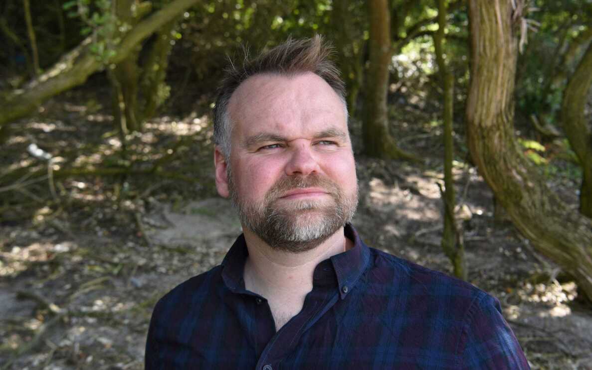 Headshot of David Atkinson standing in the woods, looking into the distance