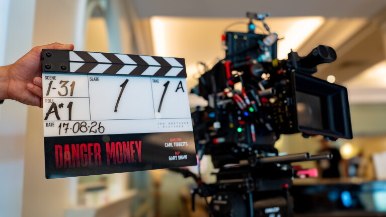 A man holding the Danger Money Clapperboard in front of a film camera.