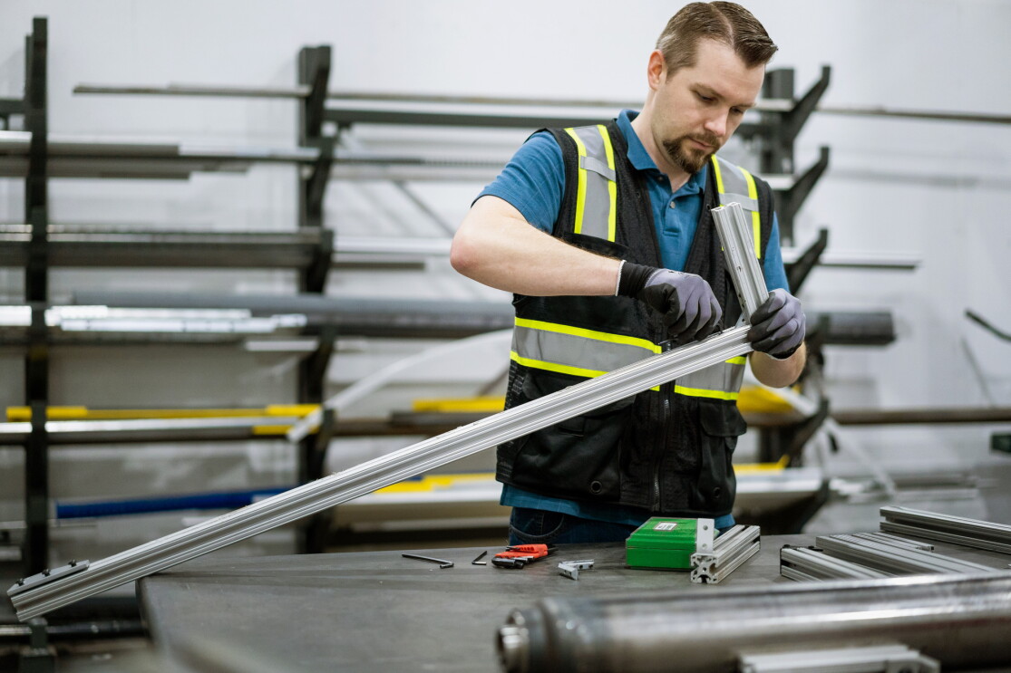 A man in a safety vest assembles a metal device.
