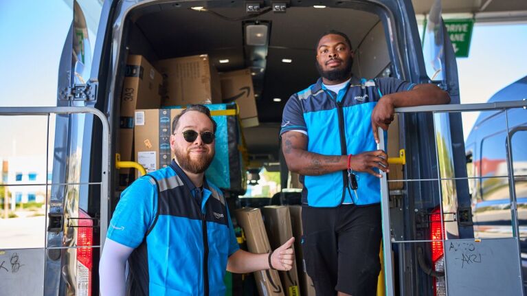 An image of two Amazon delivery drivers standing at the back of a van.