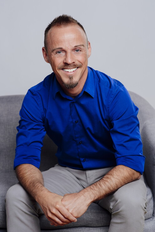 Ein Mann mit blauem Hemd und kurzen Haaren lacht in die Kamera.