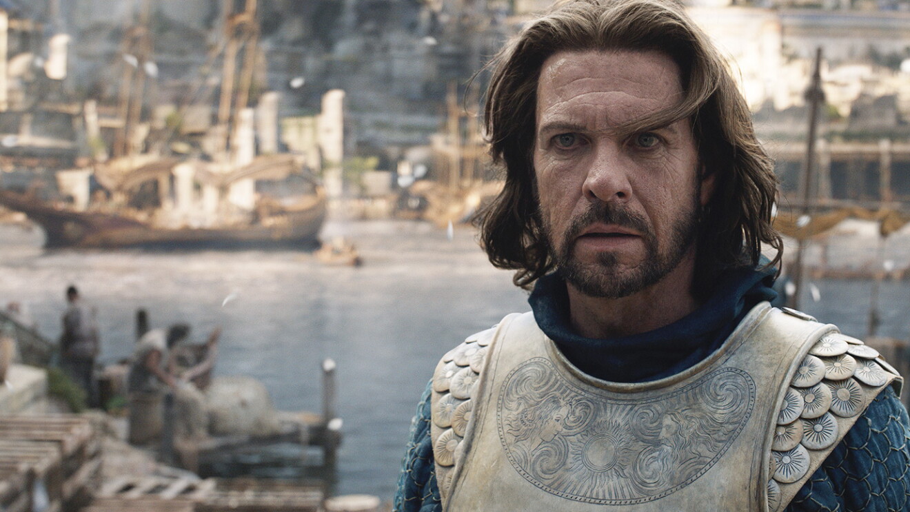 Elendil stares off into the distance toward the camera while walking from the sea.