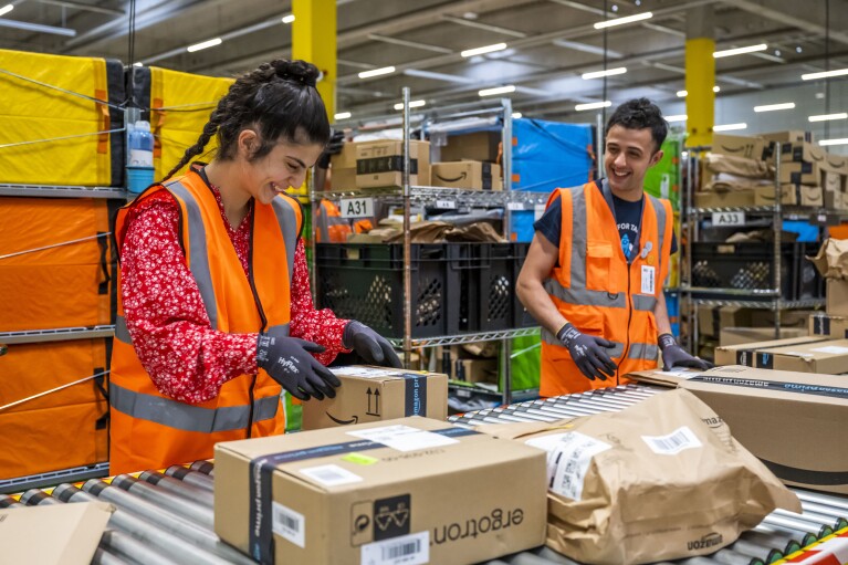 Eine Amazon Mitarbeiterin und ein Mitarbeiter an einer Förderanlage mit Paketen.