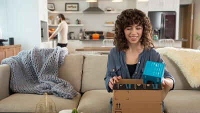 An Amazon customer smiles as they unbox a package on their couch.