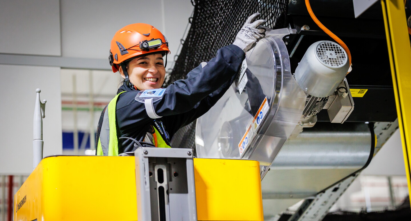 Mujer trabajando arreglando una máquina dentro de un centro logístico. 