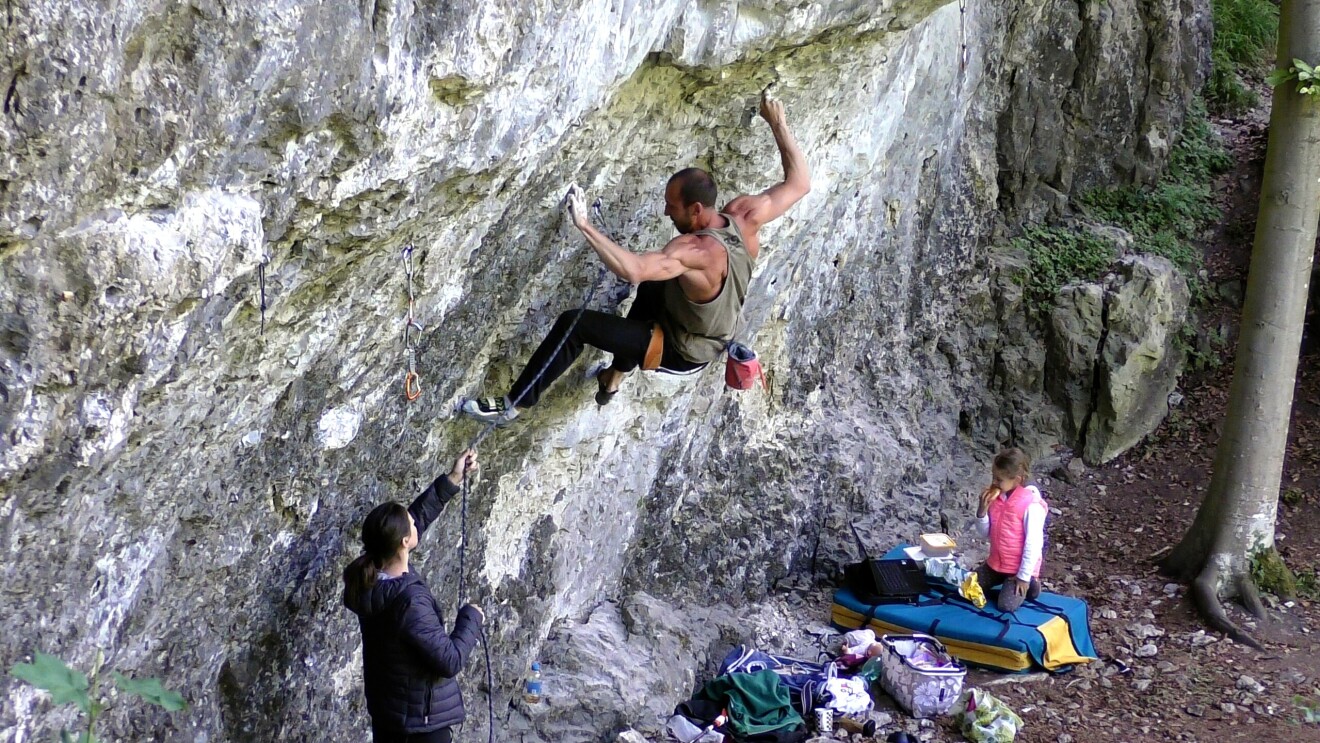 Ein Mann klettert an einer Steinwand und wird dabei von einer Frau gesichert.