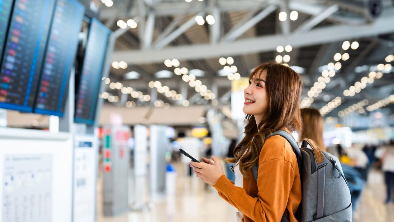 An image of a woman in an airport looking at flight schedules on TV screens.