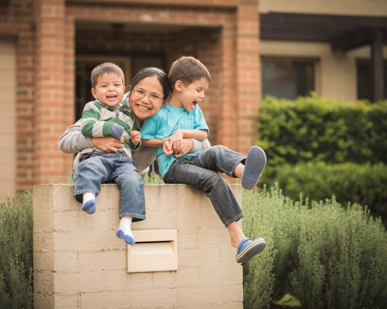 A family of a mom hugs her two boys while smiling for a photo outside of their home.