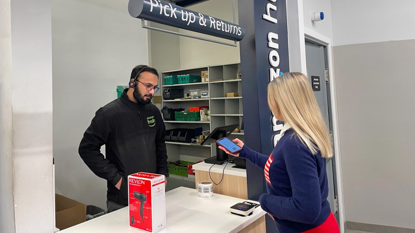 A blonde woman showing a phone with a qr code on to a store associate at an Amazon Fresh store 