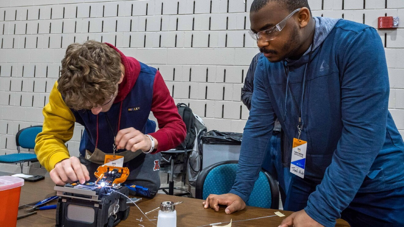 A photo of two students learning to use a fiber optic fusion splicer.