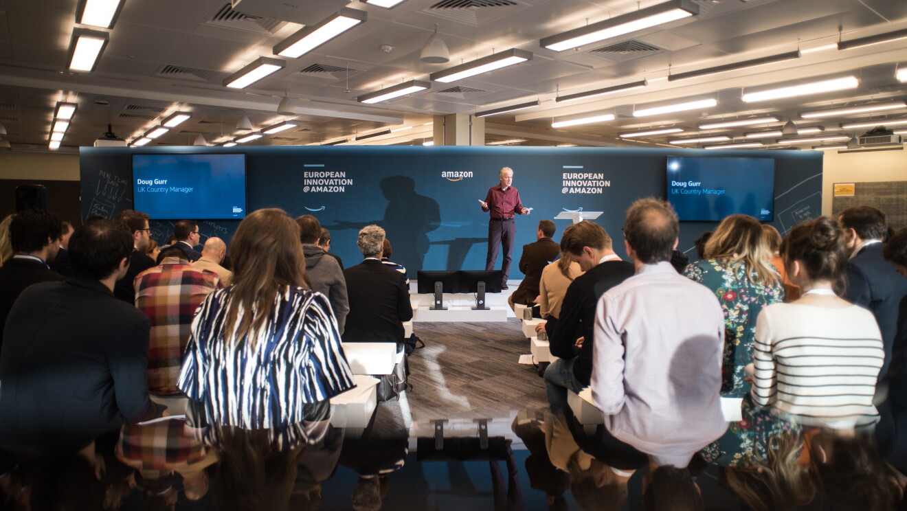 Doug Gurr, UK Country Manager Amazon. Di fronte a lui una platea di persone di spalle rispetto alla camera 