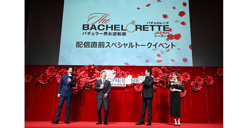 赤いバラの花の大きなオブジェと生花の赤いバラが飾られた赤い壁を背に並んで立つ4人の人物。上方のスクリーンに「配信直前スペシャルトークイベント」の文字。