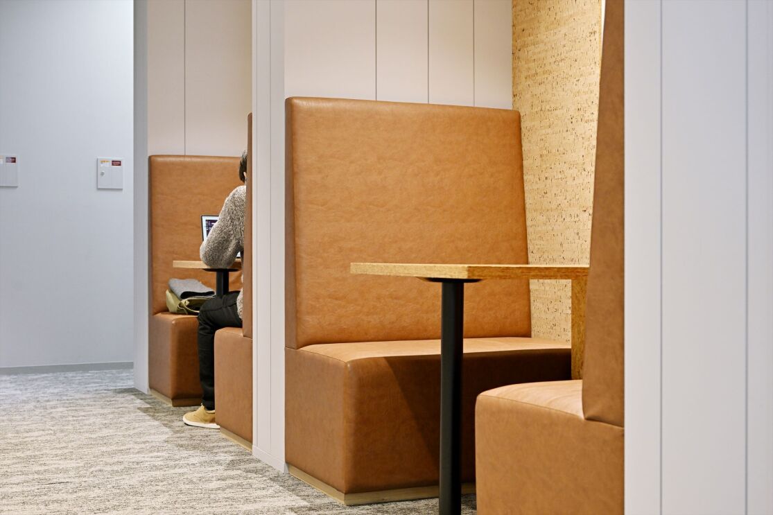 壁で区切られている空間2つには、オレンジ色のソファとハイテーブルが置かれている。その空間には男性1人がパソコンを操作している。