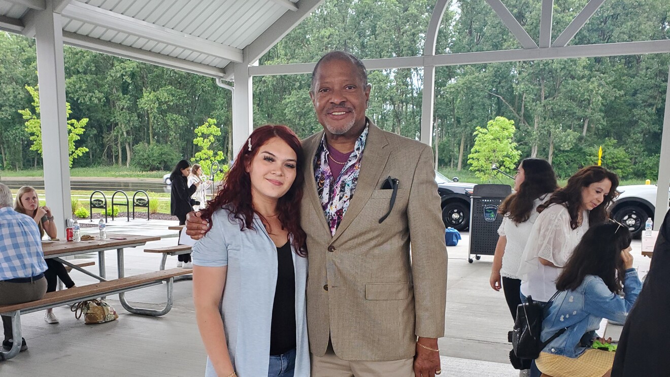 An image of a man and a woman standing together while smiling for a photo. They are at an event in a beautiful outdoor dining area.