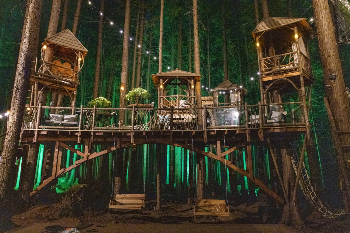 Nighttime view of series of connected wooden structures build into a forest.