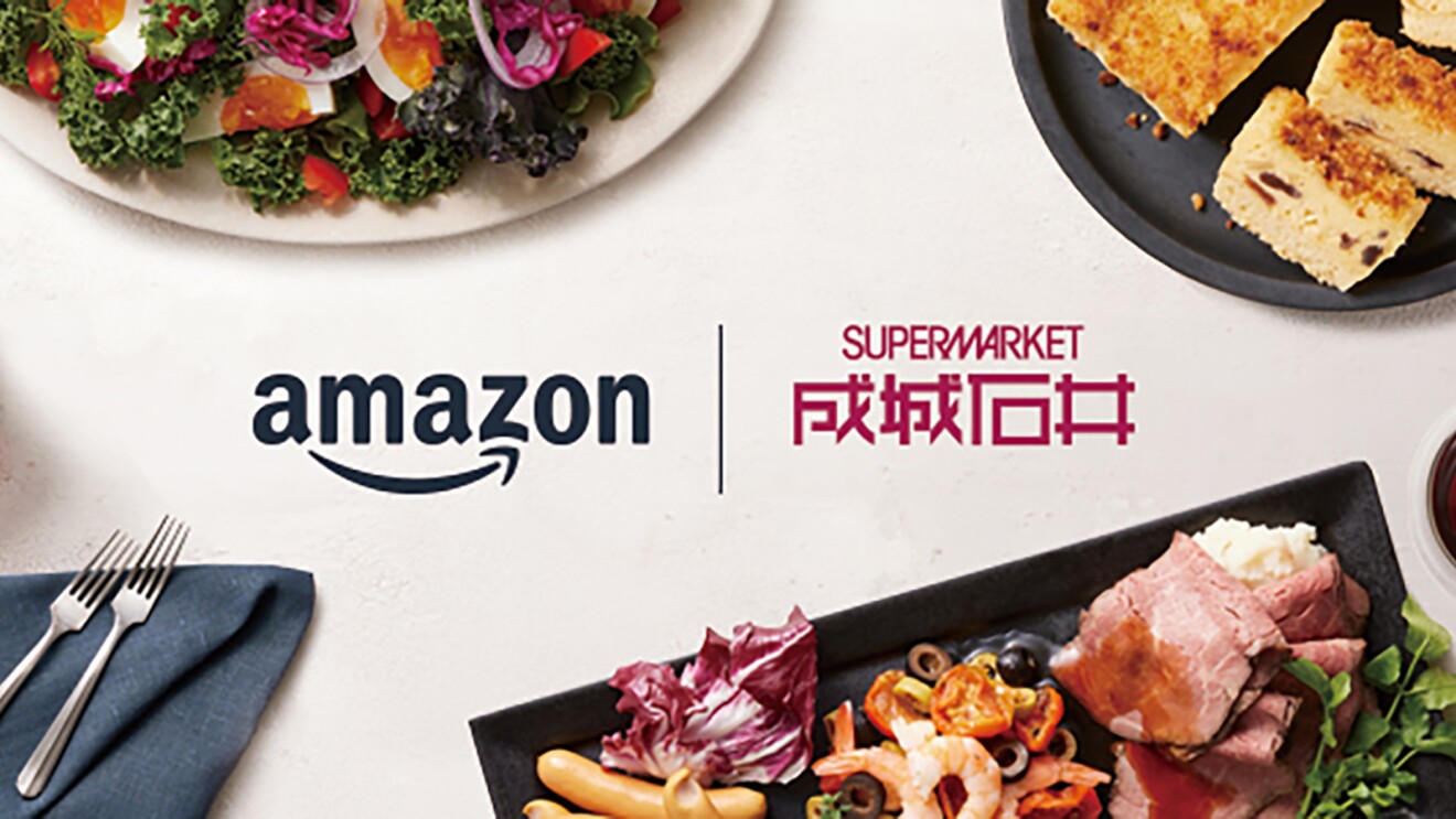 オフホワイトの背景。中央にAmazonと成城石井のロゴが横並びで配置。ロゴの上側、左の薄いベージュの丸皿には野菜サラダ、右の黒い丸皿には黄色い長方形の食べ物が盛られている。ロゴ下側には、左隅にブルーグレーのナプキンと2本のフォーク、右の黒い角皿には肉料理とマッシュポテト、付け合わせの野菜などが盛られている。