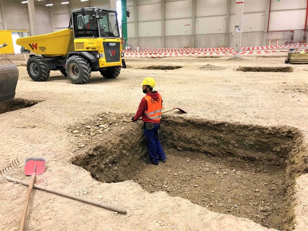 Ein Bauarbeiter steht hüfttief in einem Graben inmitten des Logistikzentrums