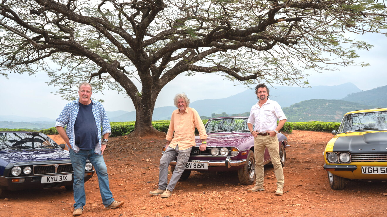 three men stand next to three vintage cars in a rural area