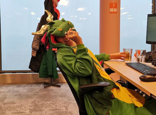 An image of Antonia sitting at her desk at her AWS office smiling while wearing a dinosaur costume.