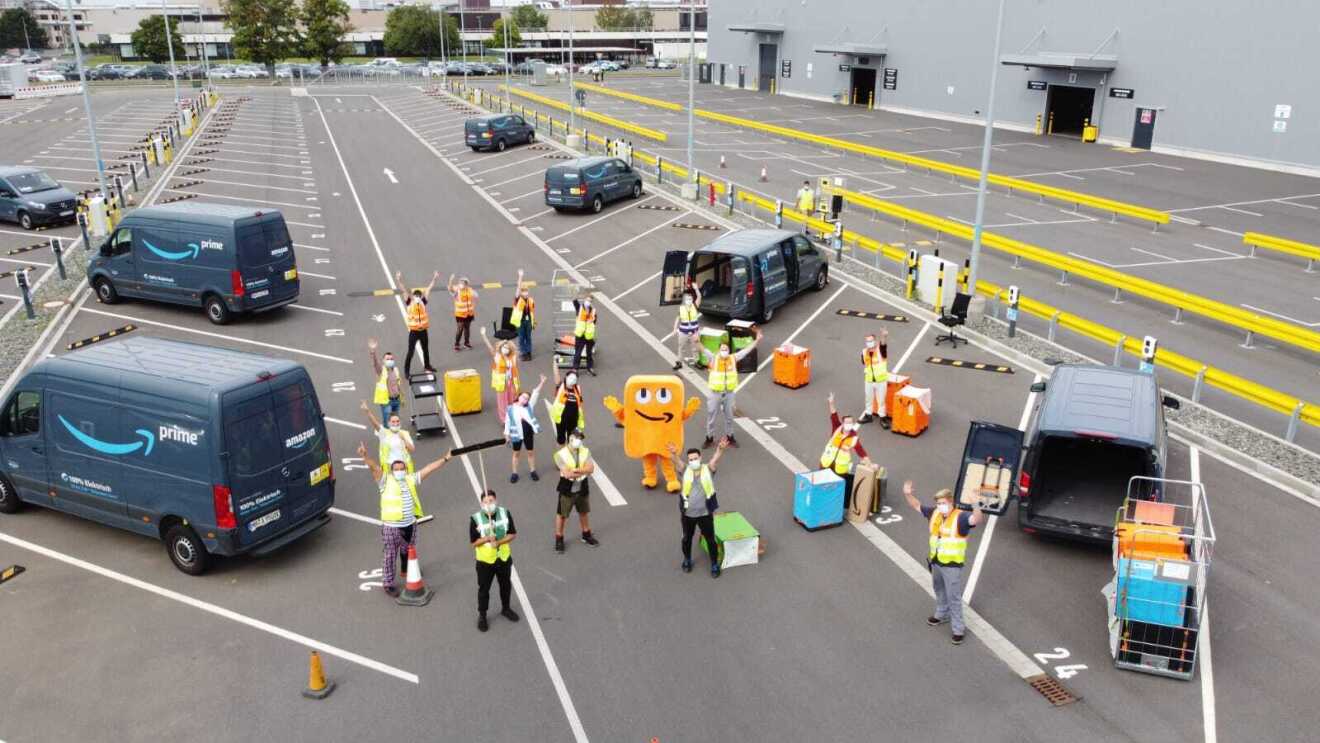 Zahlreiche Mitarbeiter:innen stehen auf dem Parkplatz des Verteilzentrums Euskirchen. Sie tragen anlässlich von "Amazon Goes Gold" ihre Schlafanzüge.